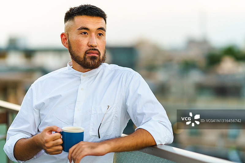年轻男子在阳台上拿着马克杯的肖像图片素材