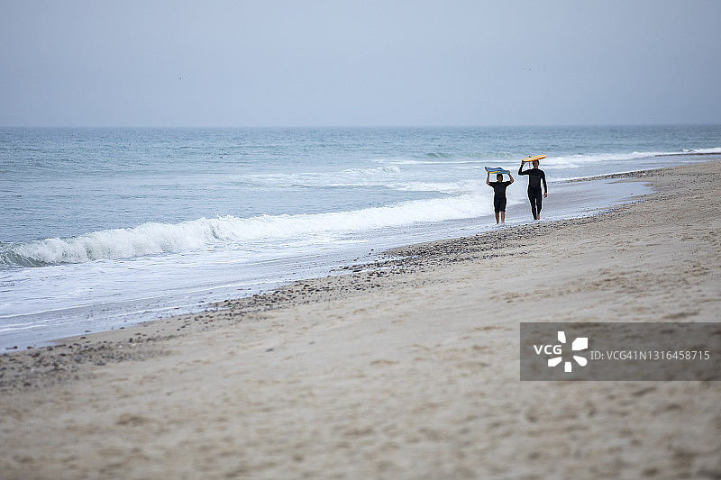 母子在远处走下海滩，带着冲浪板图片素材