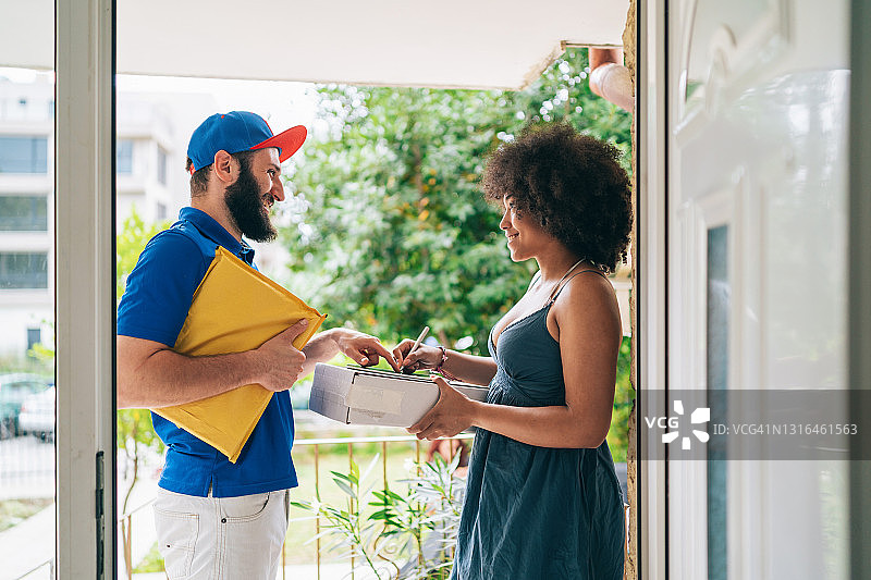 送货员在门口将小盒子送到顾客手中。女人在家收邮件图片素材