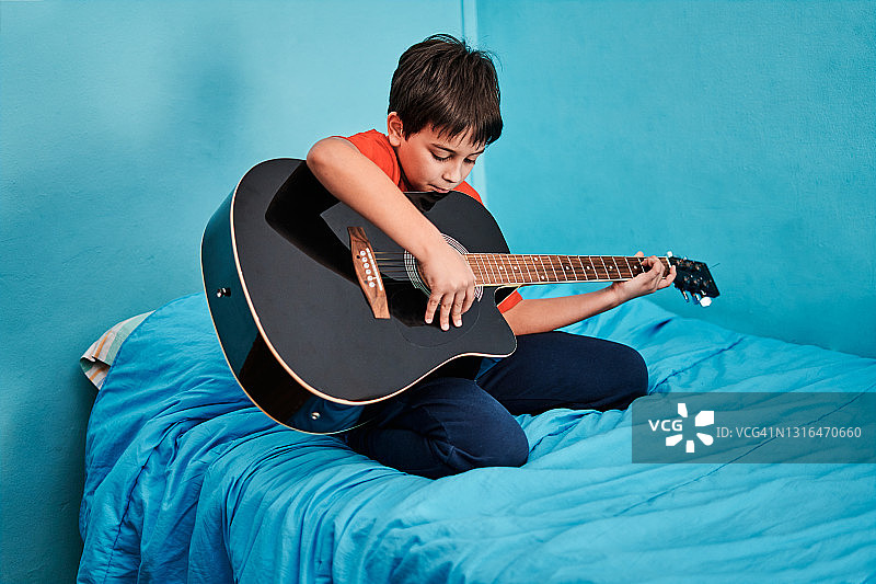 男孩在卧室的床上弹吉他图片素材