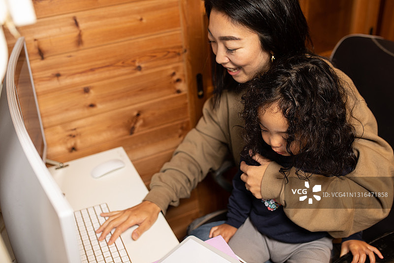 单身母亲在家用电脑工作，带着年幼的孩子图片素材