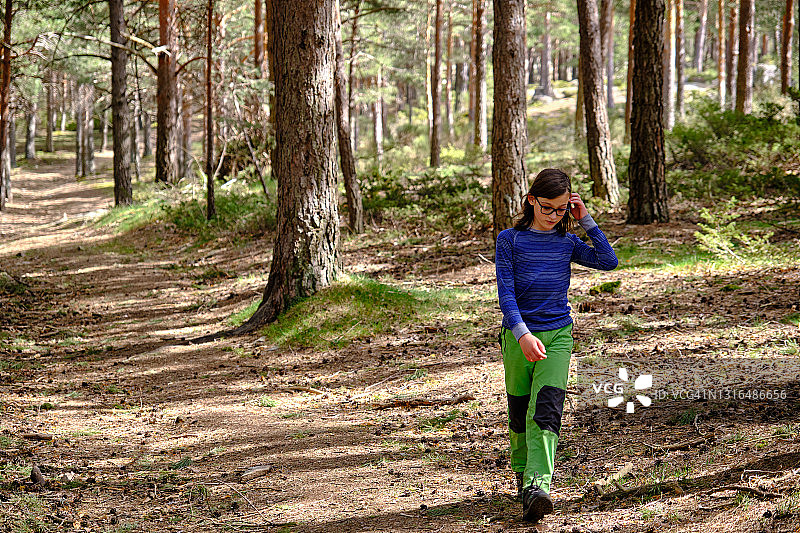 戴眼镜留长发的小男孩独自在森林里行走图片素材