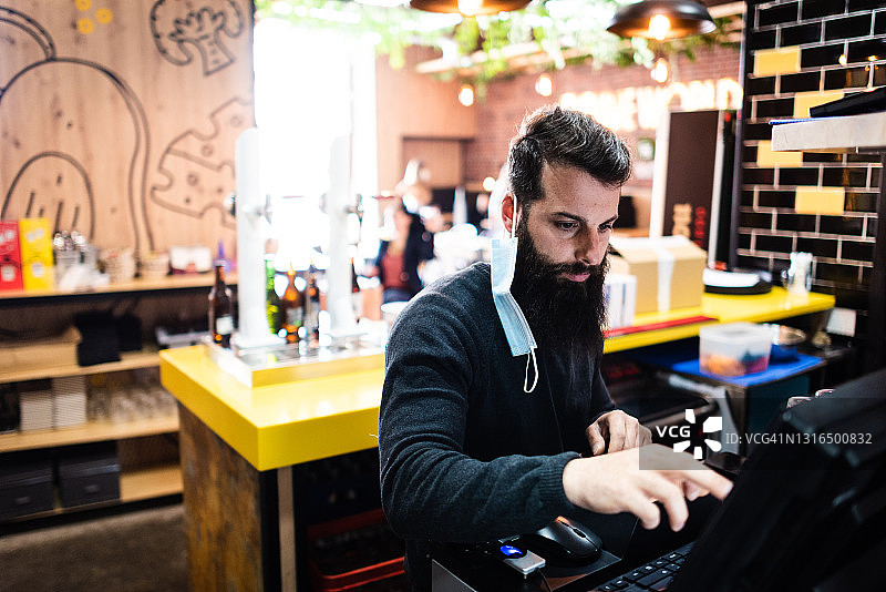 在餐厅收银台提供服务的络腮胡年轻人图片素材