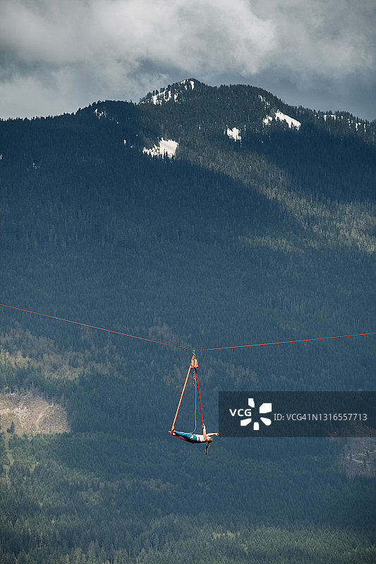 高空表演者仰卧在森林上空的绸缎上保持平衡图片素材