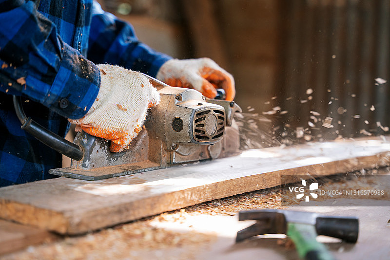 木匠在建筑工地使用电动刨床刨木板特写图片素材