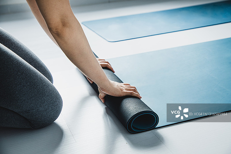 亚洲女人在瑜伽馆里卷瑜伽垫图片素材