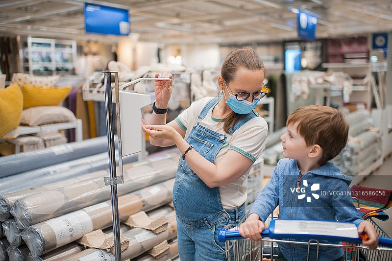 戴着防护口罩的孕妇和她的儿子在购物中心使用洗手液图片素材