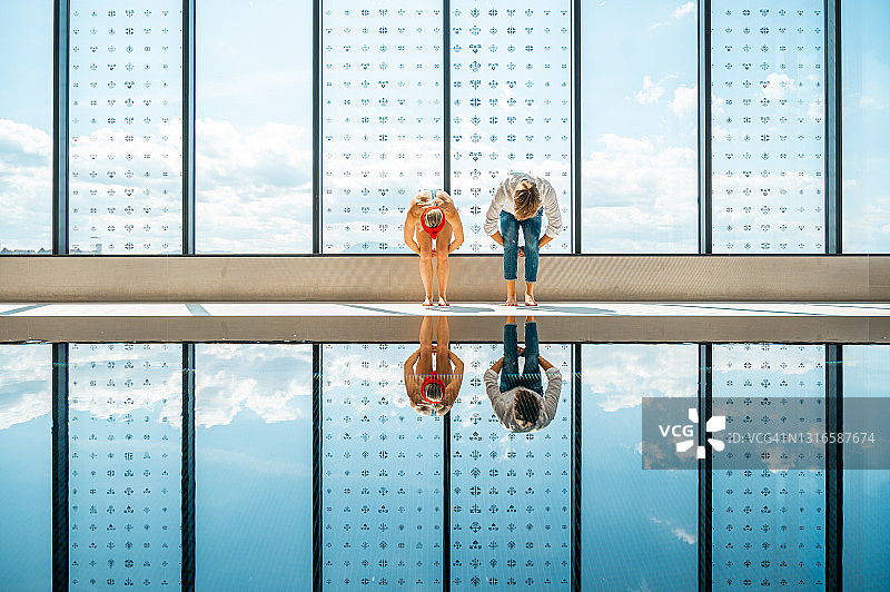 年轻情侣在室内游泳池旁弯腰图片素材