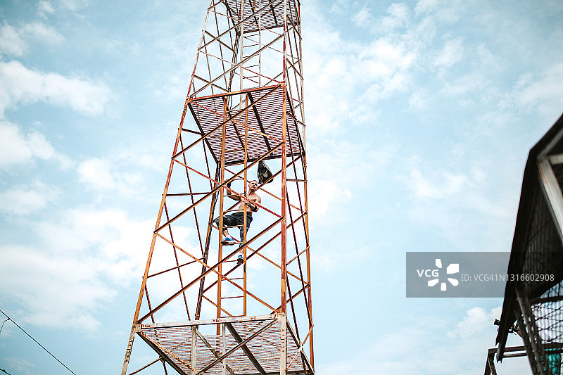在塔上爬梯子的健壮赤膊男人图片素材
