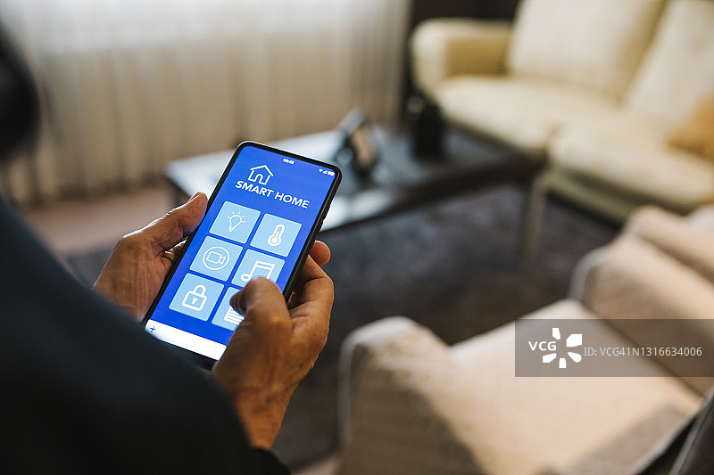 年长的女人在家里的客厅里使用手机上的智能家居应用程序图片素材