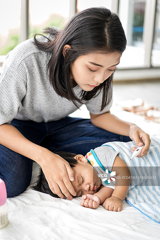 母亲在家用电子体温计小心地照顾她的宝宝图片素材