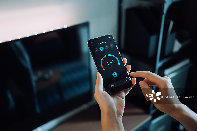 女人用智能手机设置智能家居系统，遥控智能空调的恒温器图片素材