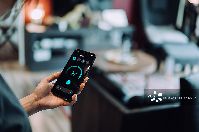 年轻亚洲女性用手机设置智能家居系统，远程控制客厅智能照明亮度图片素材