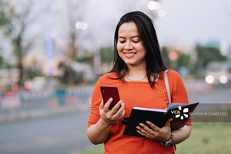 看着镜头、拿着书和使用手机的印度少女图片素材