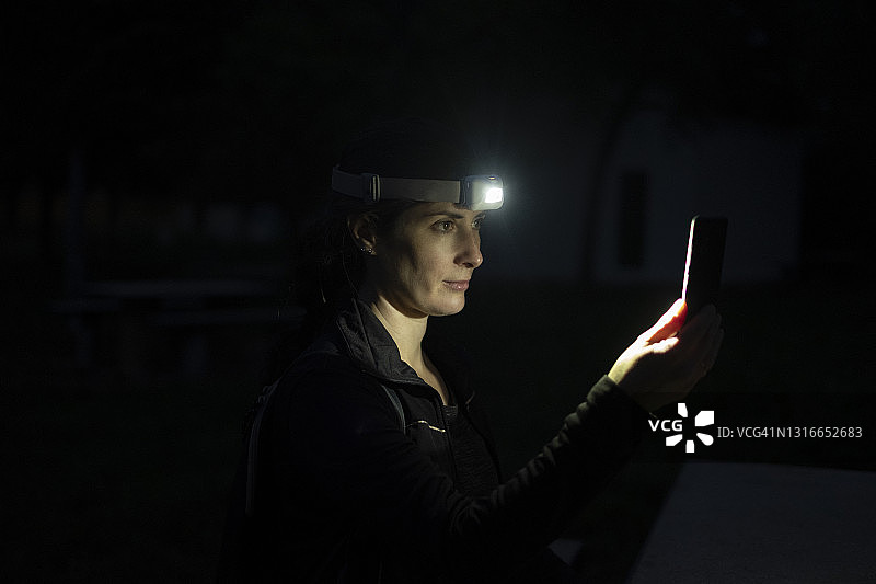 迷人的女士开启夜间徒步，查看手机图片素材