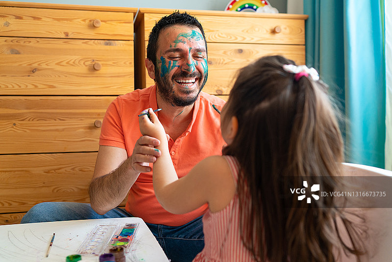 脸上涂着油彩，对着小女儿微笑的年轻英俊父亲图片素材