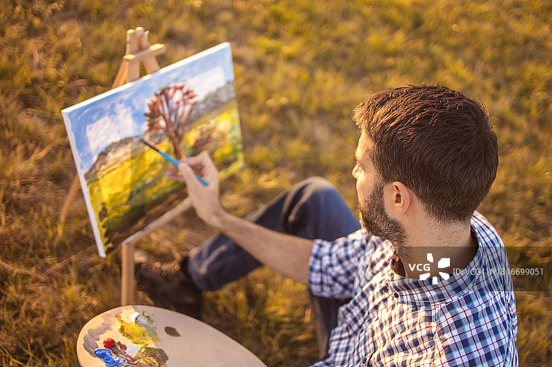 年轻男人在日落时于大自然中在画布上绘画图片素材
