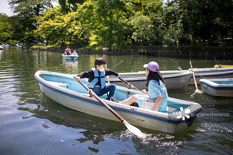 戴口罩的亚洲儿童在公园里划船图片素材