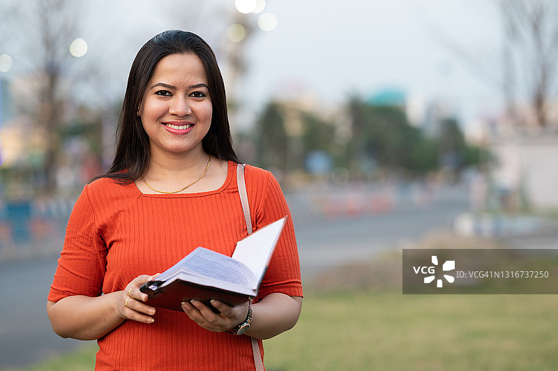 美丽的印度少女看向镜头手捧书本微笑图片素材