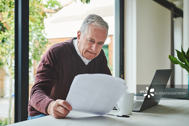 一位年长的男人独自坐在家里，用笔记本电脑计算财务图片素材