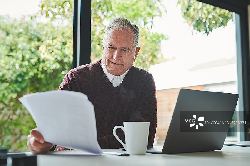 一位年长的男人独自坐在家里，用笔记本电脑计算财务图片素材