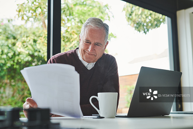 一位年长的男人独自坐在家里，用笔记本电脑计算财务图片素材