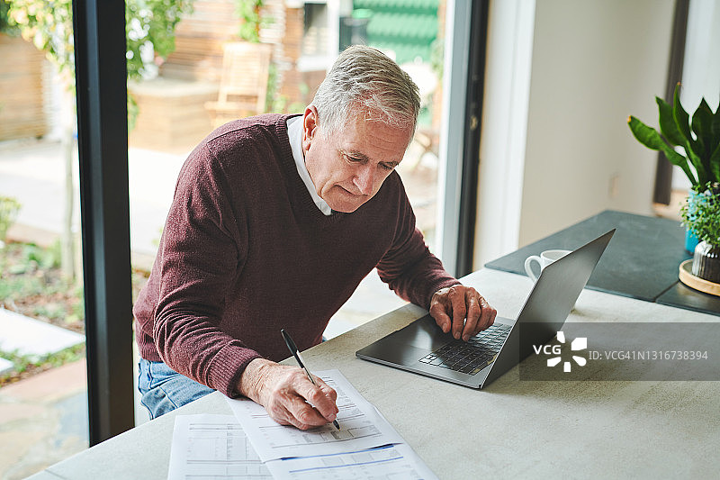 一位年长的男人独自坐在家里，用笔记本电脑计算财务图片素材