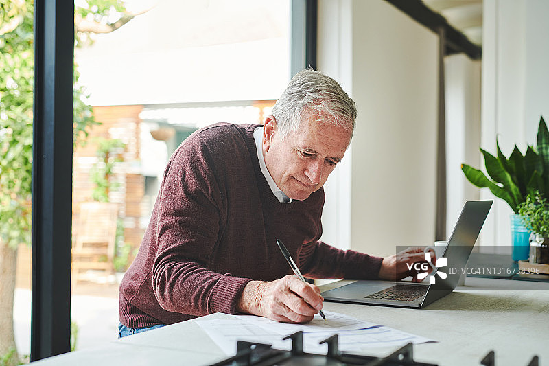 一位年长的男人独自坐在家里，用笔记本电脑计算财务图片素材