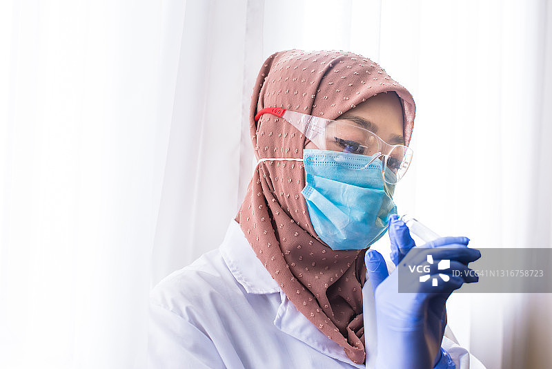 戴着头巾和防护手套的穆斯林女科学家在实验室检查COVID-19测试盒图片素材