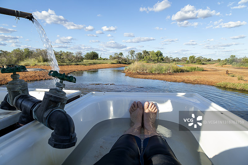 一人坐在户外的浴缸里，腿部特写，水从河床流下图片素材
