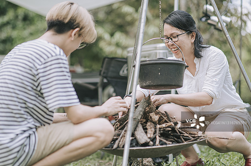 中国男孩和母亲在帐篷旁准备晚餐，生火煮汤图片素材