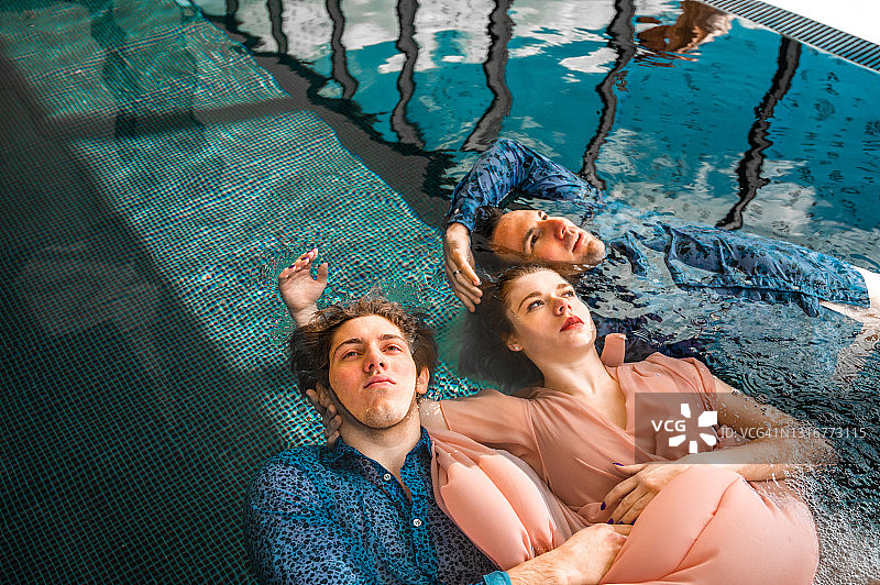 三个年轻人在泳池里穿着衣服漂浮在水上图片素材