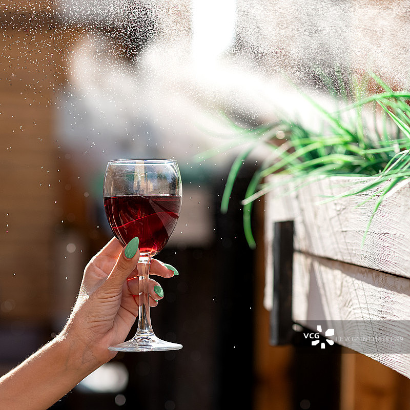 女人手持装有红酒的玻璃杯，背景模糊，水滴飞溅。酒精饮料图片素材