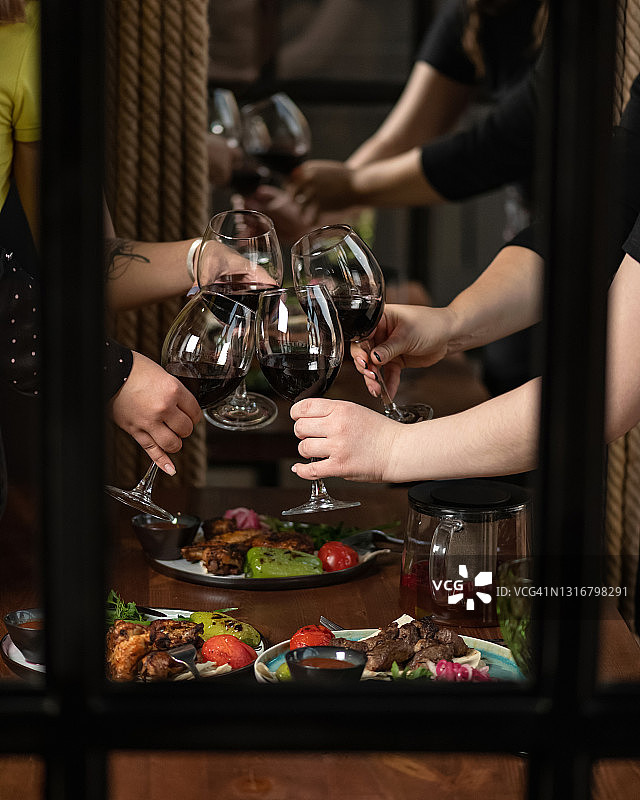 女士们举起红酒杯碰杯庆祝。在餐厅的节日晚餐上友好祝酒。一群女性一起庆祝活动，隔着窗户拍摄。酒精饮料图片素材