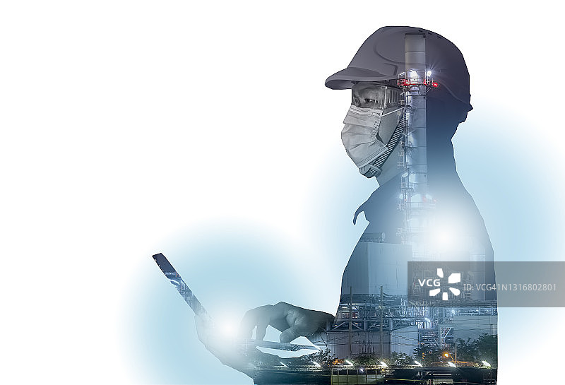 工程师戴口罩防新冠，手按电脑，炼油厂作业，系统和背景图的双重曝光。大型炼油厂夜间作业。石油工业工程师概念图片素材