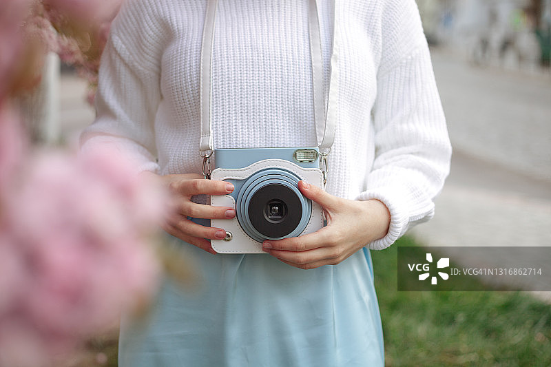 在户外春天拿着蓝色复古相机站在樱花树附近的年轻女子图片素材
