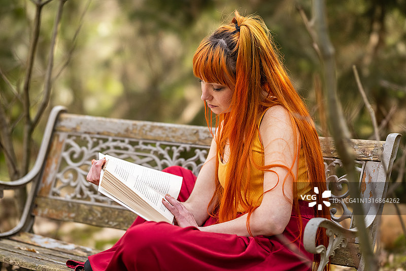 坐在自然风光中的长椅上，放松地阅读经典小说的年轻女人图片素材