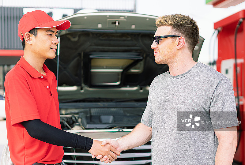 白人车主与亚洲加油站员工握手，成功完成汽车发动机维护并在加油站为汽车油箱加注燃料图片素材