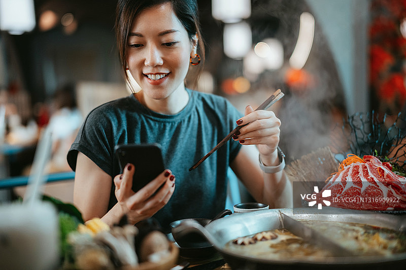 年轻亚洲女子在餐厅享用美味的中国传统火锅图片素材
