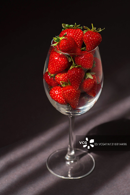 黑色背景下，盛在红酒杯中的成熟草莓图片素材