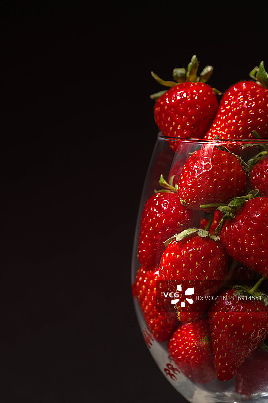 黑色背景下，盛在红酒杯中的成熟草莓图片素材