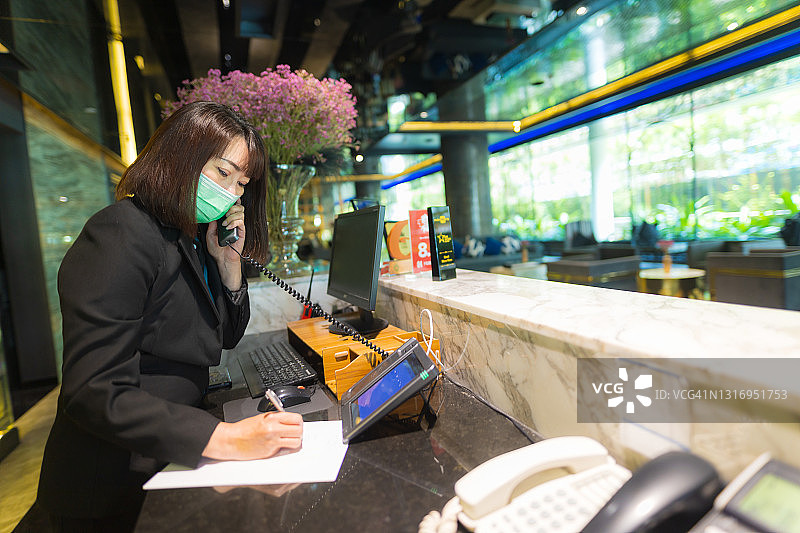 亚洲酒店前台接待员正在酒店大堂打电话图片素材