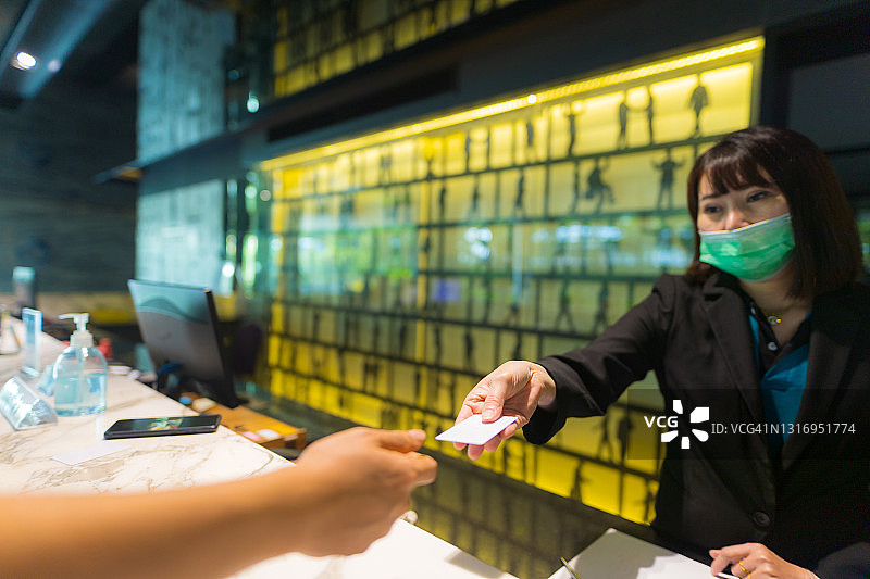 戴防护口罩的亚洲女接待员给顾客递房卡图片素材