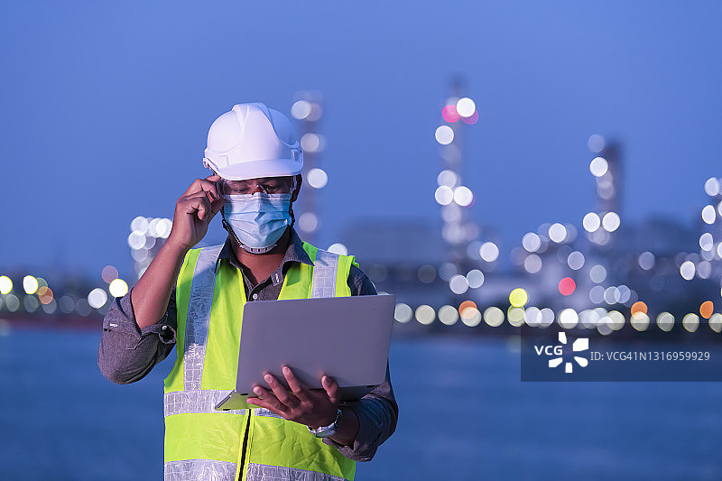 炼油厂工程师戴口罩防护，手持电脑在炼油厂工作图片素材