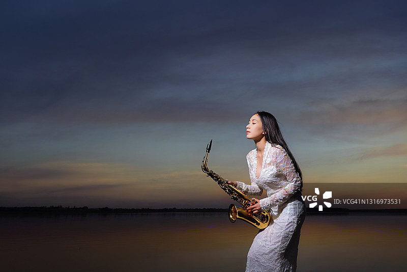 站在湖边拿着萨克斯的美丽女子肖像图片素材