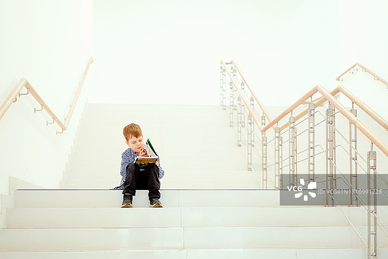 男孩在白色大楼梯上看书图片素材