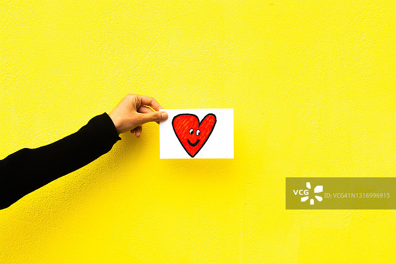 女人手拿画有感恩之心的卡片，黄色背景图片素材