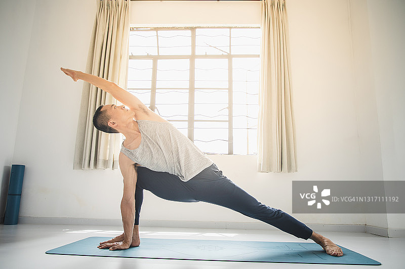 在瑜伽馆里做瑜伽伸展侧角式的亚洲男人图片素材