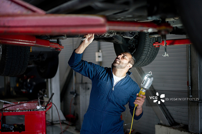 在修理厂工作，拿着灯检查汽车底盘的维修工图片素材