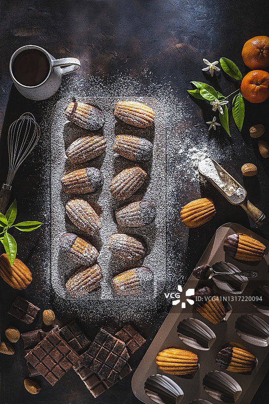 自制玛德琳，模具中融化的巧克力，撒上糖粉，深色木纹背景图片素材